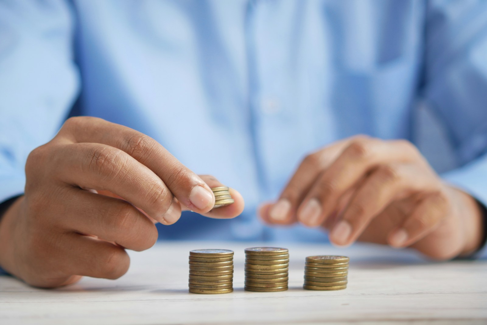 A person stacks coins into organized piles, emphasizing financial management and saving strategies. The setting suggests a focus on personal finance.