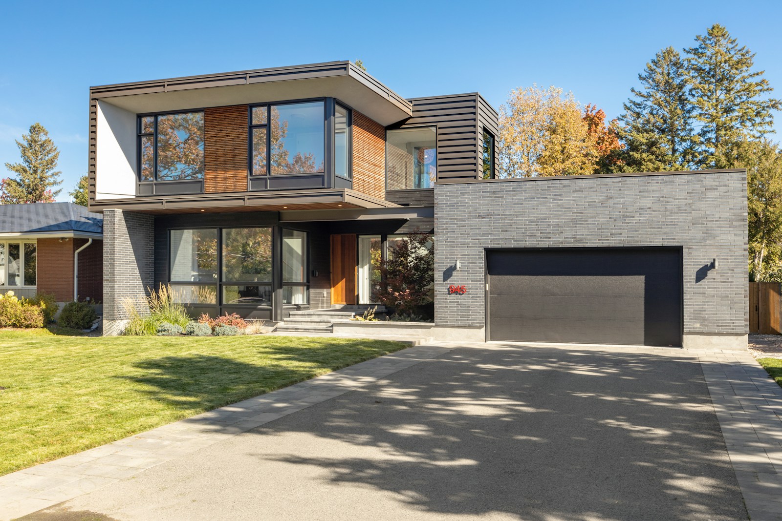 Modern two-story house with large windows, a sleek gray brick exterior, and a landscaped front yard. Ideal example of contemporary architecture.